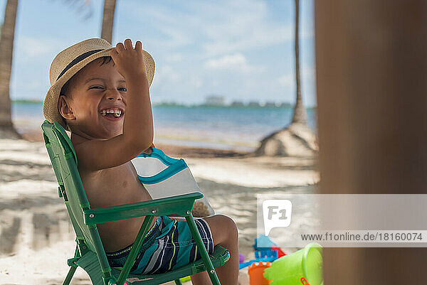 Kleine lateinische Baby Junge trägt einen Hut am Strand sitzen und lächelnd