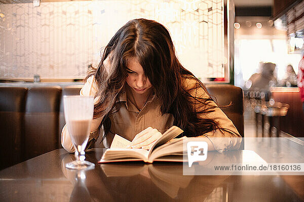Teenager-Mädchen  das in einem Café sitzt und ein Buch liest