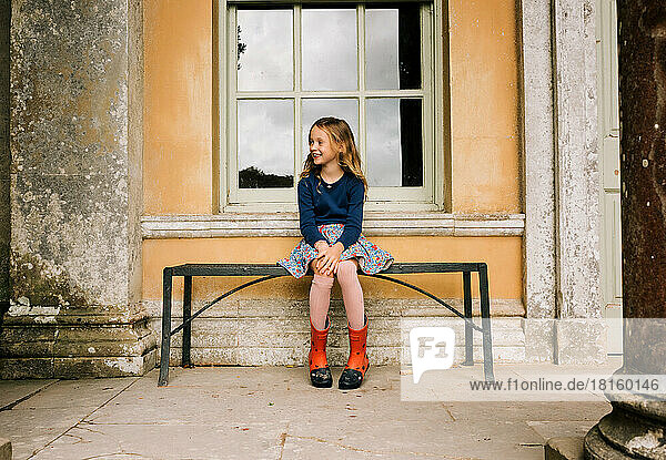 Mädchen sitzt glücklich auf einer Bank vor einem Schloss in England