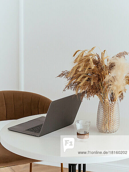 Laptop auf einem weißen Tisch mit einer Vase und einem Herbststrauß