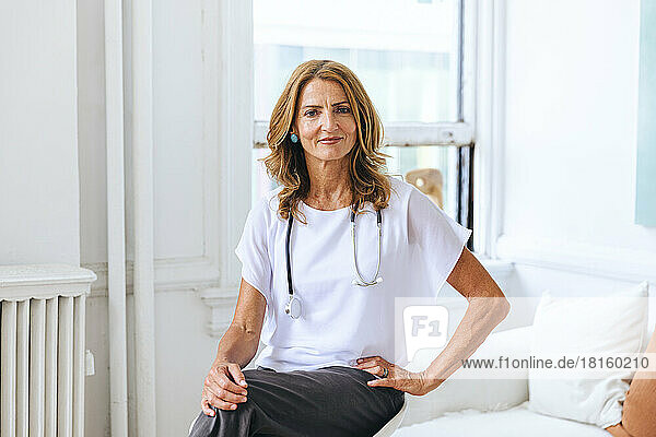 Porträt einer selbstbewussten Ärztin  die auf einem Tisch im Krankenhaus sitzt