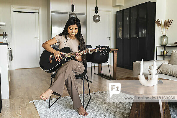 Young woman playing guitar sitting at home