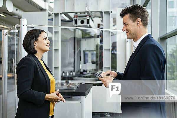 Smiling businessman holding tablet PC looking at businesswoman in industry