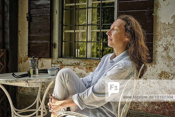Mature woman sitting with eyes closed on terrace in morning