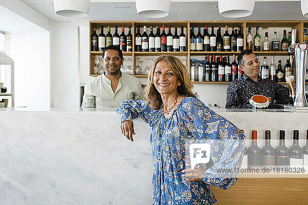 Happy businesswoman with bartenders standing at bar counter in restaurant