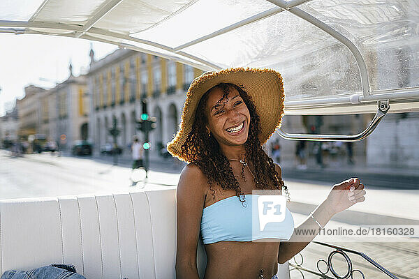 Cheerful young woman wearing hat taking tuk tuk ride on sunny day