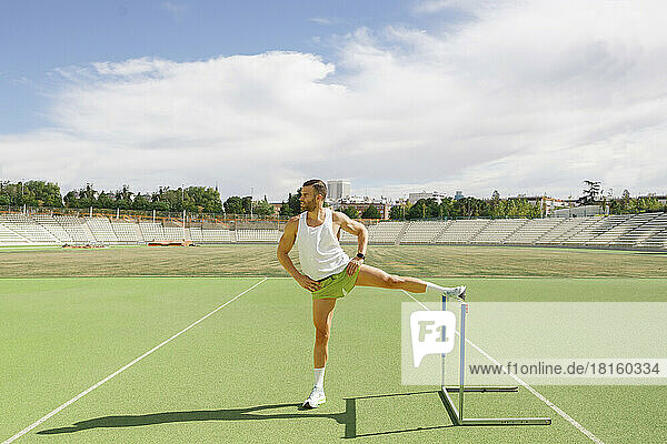 Sportsman doing warm up exercise by hurdle on running track