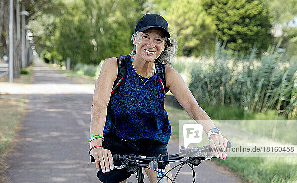 Happy senior woman wearing cap riding bicycle on footpath