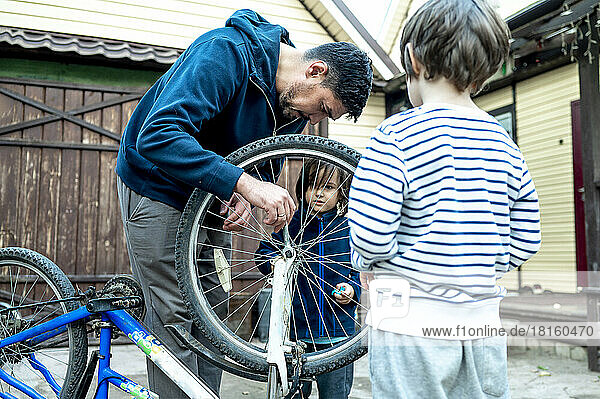 Man repairing wheel of bicycle by sons outside house