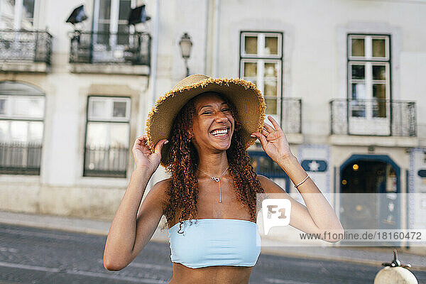 Happy young woman wearing hat in front of building