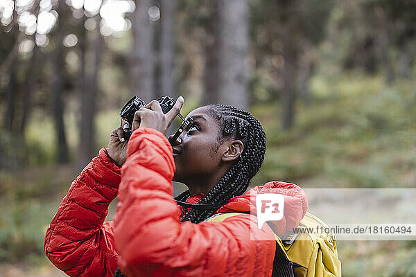 Young woman with braided hair photographing in forest