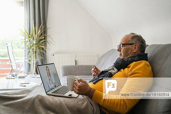 Älterer Mann führt Videoanruf mit Arzt über Laptop  sitzt zu Hause auf dem Sofa