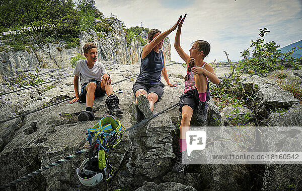 Boy looking at mother giving high five to girl on rock
