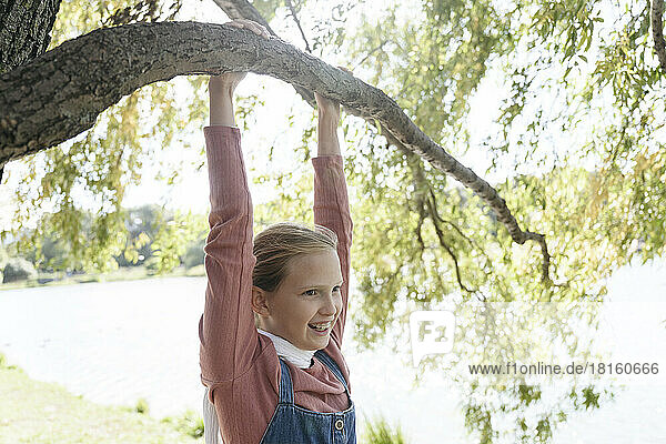Smiling girl hanging on tree branch in park