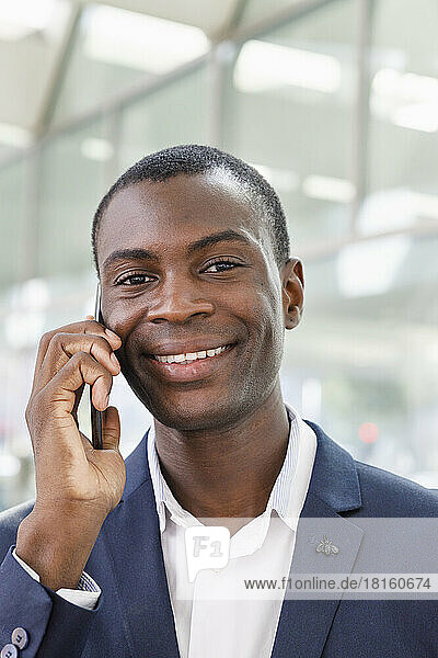 Happy young businessman talking on smart phone at railroad station