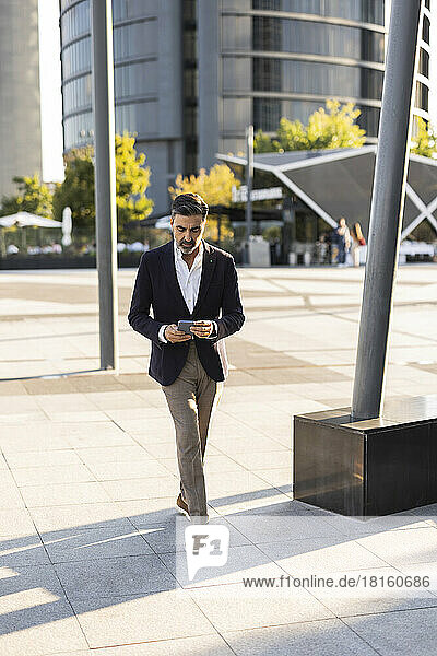 Businessman using smart phone walking on footpath