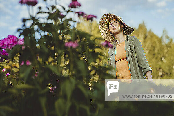 Smiling woman with hat day dreaming in garden