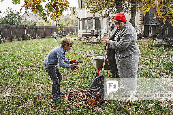 Mother with son raking dry leaves in back yard