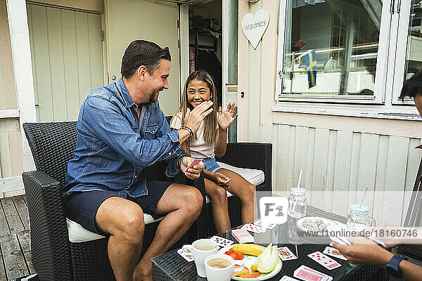 Vater und Tochter geben sich gegenseitig High Five und sitzen auf einem Stuhl auf der Veranda
