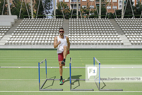 Athlete doing exercise near hurdles on sunny day
