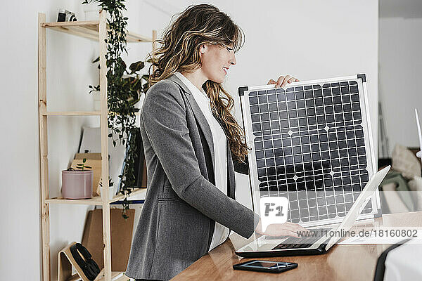 Moderne Geschäftsfrau arbeitet am Laptop und nutzt tragbares Solarmodul im Büro