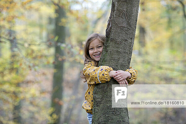 Happy cute girl hugging tree in forest