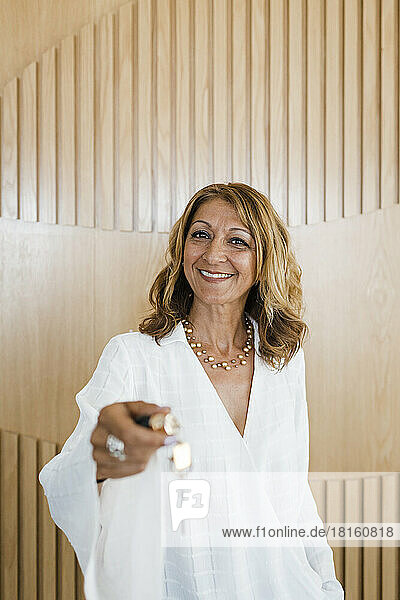 Happy mature businesswoman giving keys standing in front of wooden wall