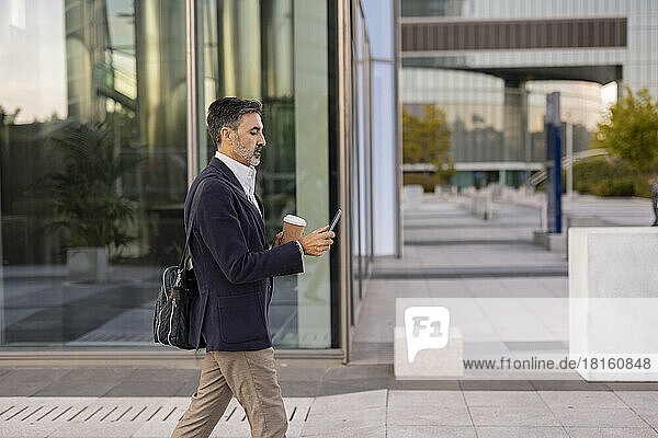 Businessman using smart phone walking in front of office building