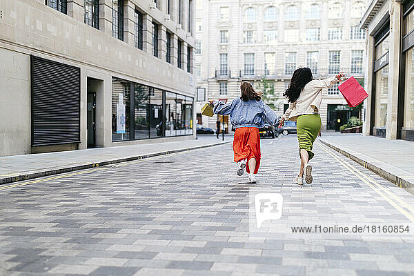 Carefree lesbian friends with shopping bags running on footpath