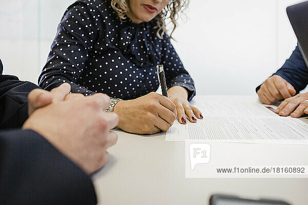 Mature businesswoman doing signature on document at desk