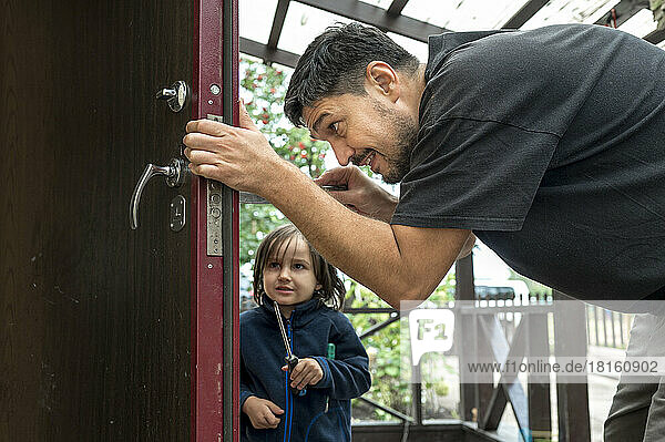 Man repairing door with son in background