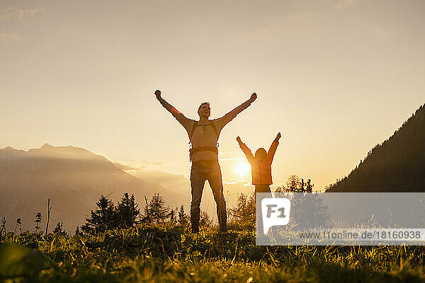 Man with daughter rising fist on top of mountain at sunset