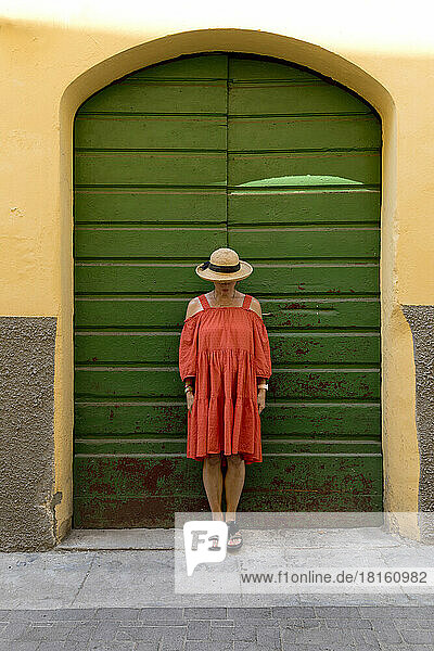 Senior woman wearing red dress and sun hat in front of green door