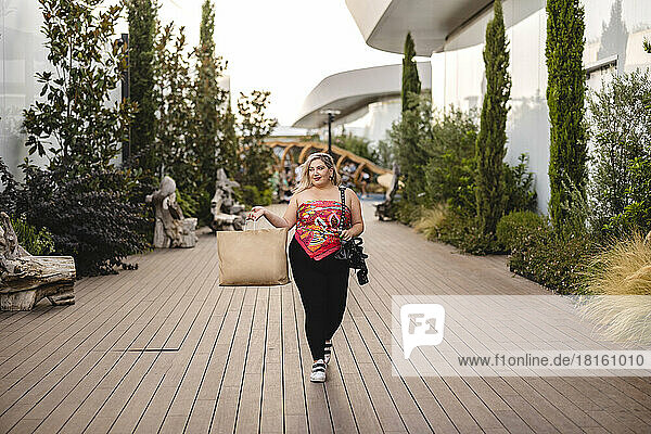 Smiling young woman carrying shopping bag walking on footpath