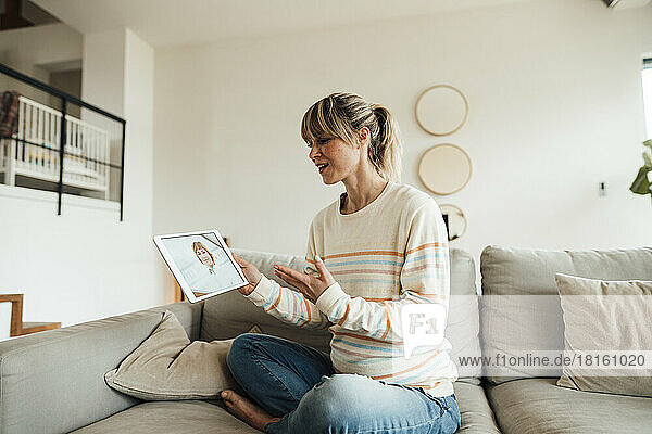 Pregnant woman discussing with doctor through tablet PC sitting on sofa at home