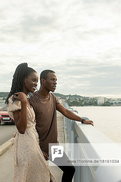 Smiling woman with boyfriend standing by railing looking at river