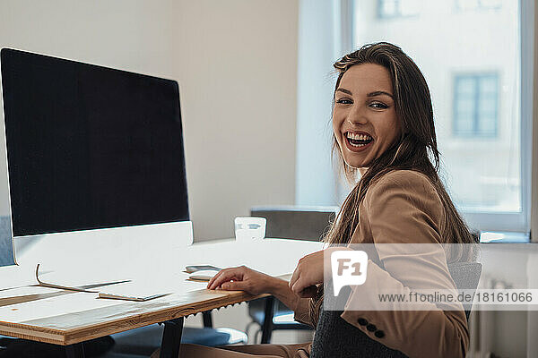 Cheerful young freelancer sitting in front of desktop PC at home office