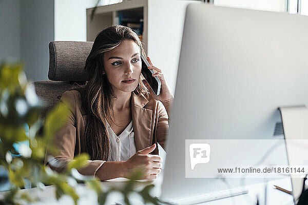 Young businesswoman talking on mobile phone in front of desktop PC