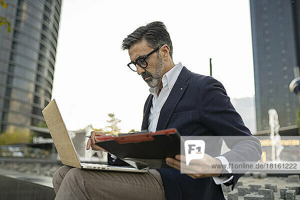 Businessman with clipboard working on laptop