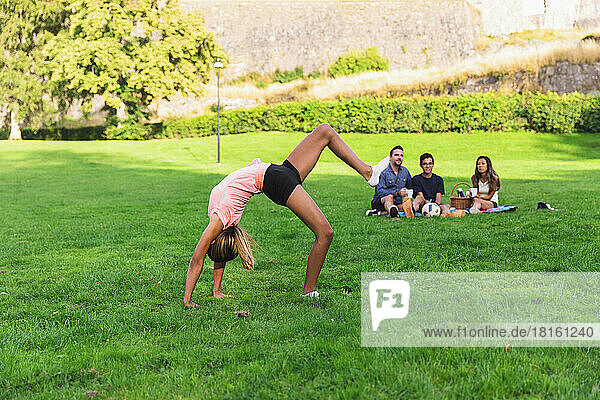 Girl doing acrobatics with family sitting in background at picnic