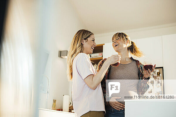 Happy pregnant woman enjoying drink with sister at home
