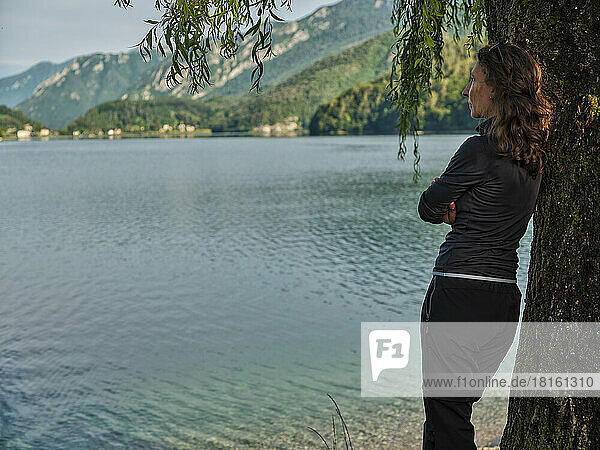 Mature woman leaning on tree at lakeshore