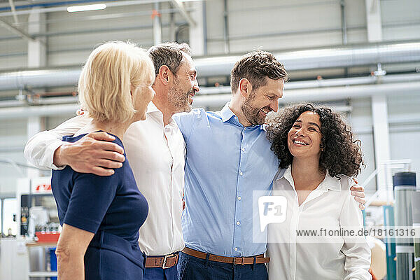 Happy business colleagues standing with arms around in industry