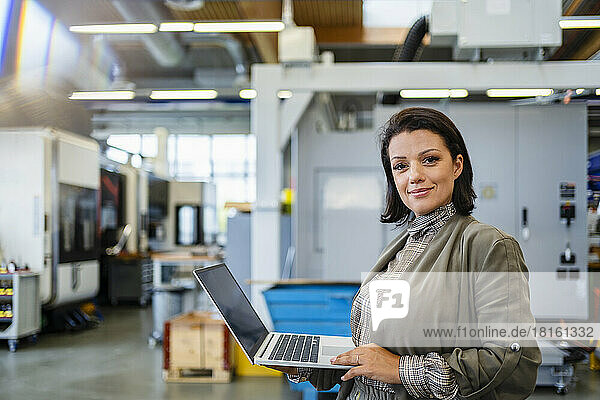 Smiling mature businesswoman holding laptop in industry