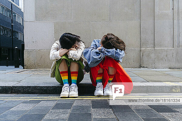 Junges lesbisches Paar mit auf Armen ruhendem Kopf sitzt zusammen am Fußweg