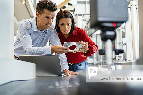 Mature colleague with technician analyzing machine part at factory