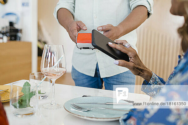 Reife Geschäftsfrau  die im Restaurant per Smartphone bezahlt