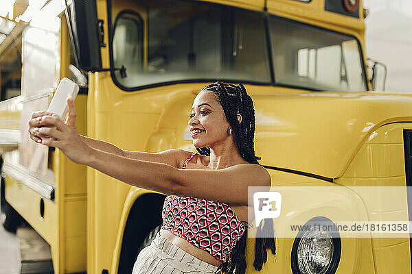 Lächelnde Frau macht ein Selfie mit ihrem Smartphone und stützt sich auf einen Imbisswagen
