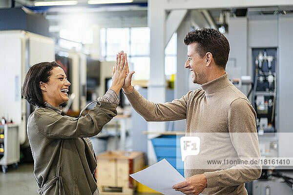 Happy businessman giving high five to businessman holding document in production hall