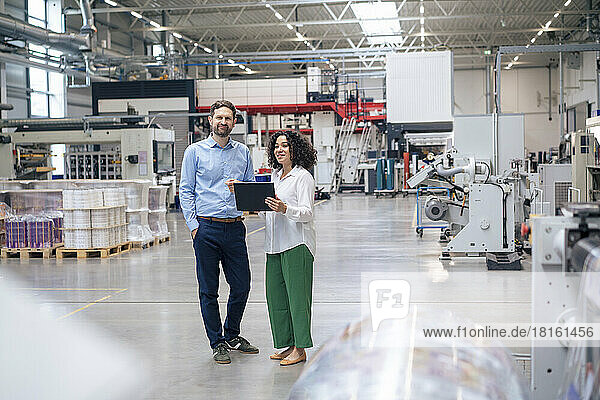 Smiling businesswoman with tablet PC standing by businessman in factory